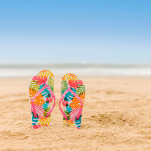 Slippers staan rechtop in het zand op een zonnig strand, met op de achtergrond zee en een helderblauwe lucht.
