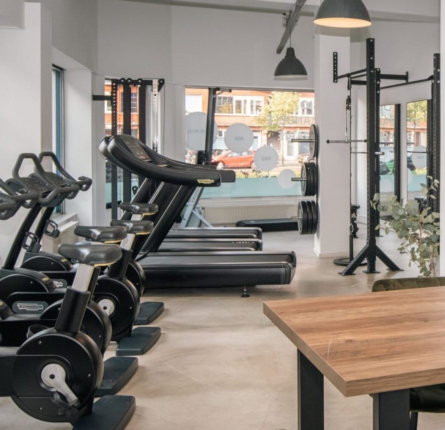 Ruime oefenzaal van F3 Fysio Rotterdam Noord voor fysiotherapie met fietsen en crosstrainers. De grote ramen kijken uit  op de Schieweg in Rotterdam 