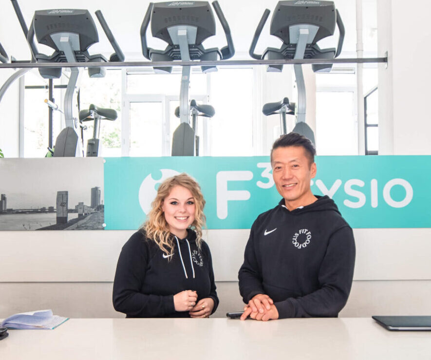 Twee medewerkers van F3 Fysio verwelkomen cliënten aan de balie van de praktijk in Rotterdam Blijdorp aan de Walenburgerweg, klaar om afspraken in te plannen.