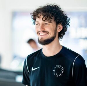 Lachende man bij F3 Fysio, gekleed in een zwart Nike T-shirt, straalt energie en motivatie uit in een professionele trainingsomgeving gericht op herstel en welzijn.