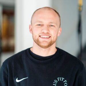 Een lachende man draagt een zwarte Nike-sweater met het Fit Food Focus-logo. De afbeelding straalt een gezonde en energieke uitstraling uit, passend bij de sfeer van F3 Fysio.