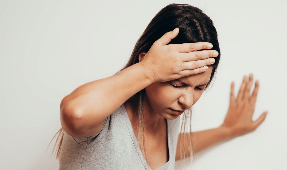 Vrouw in het grijze shirt heeft haar rechter hand op haar hoofd. Ze is duizelig en heeft las van haar hoofd. nekklachten