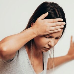 Vrouw in het grijze shirt heeft haar rechter hand op haar hoofd. Ze is duizelig en heeft las van haar hoofd. nekklachten