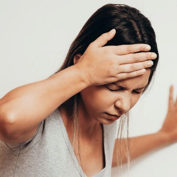 Vrouw in het grijze shirt heeft haar rechter hand op haar hoofd. Ze is duizelig en heeft las van haar hoofd. nekklachten
