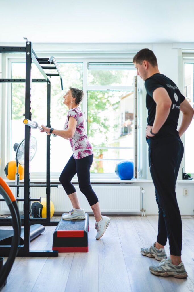 Een vrouw revalideert van een VKB-operatie en oert onder begeleiding van een trainer step-oefeningen uit in f3 fysio Rotterdam.