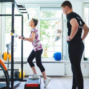 Een vrouw revalideert van een VKB-operatie en oert onder begeleiding van een trainer step-oefeningen uit in f3 fysio Rotterdam.