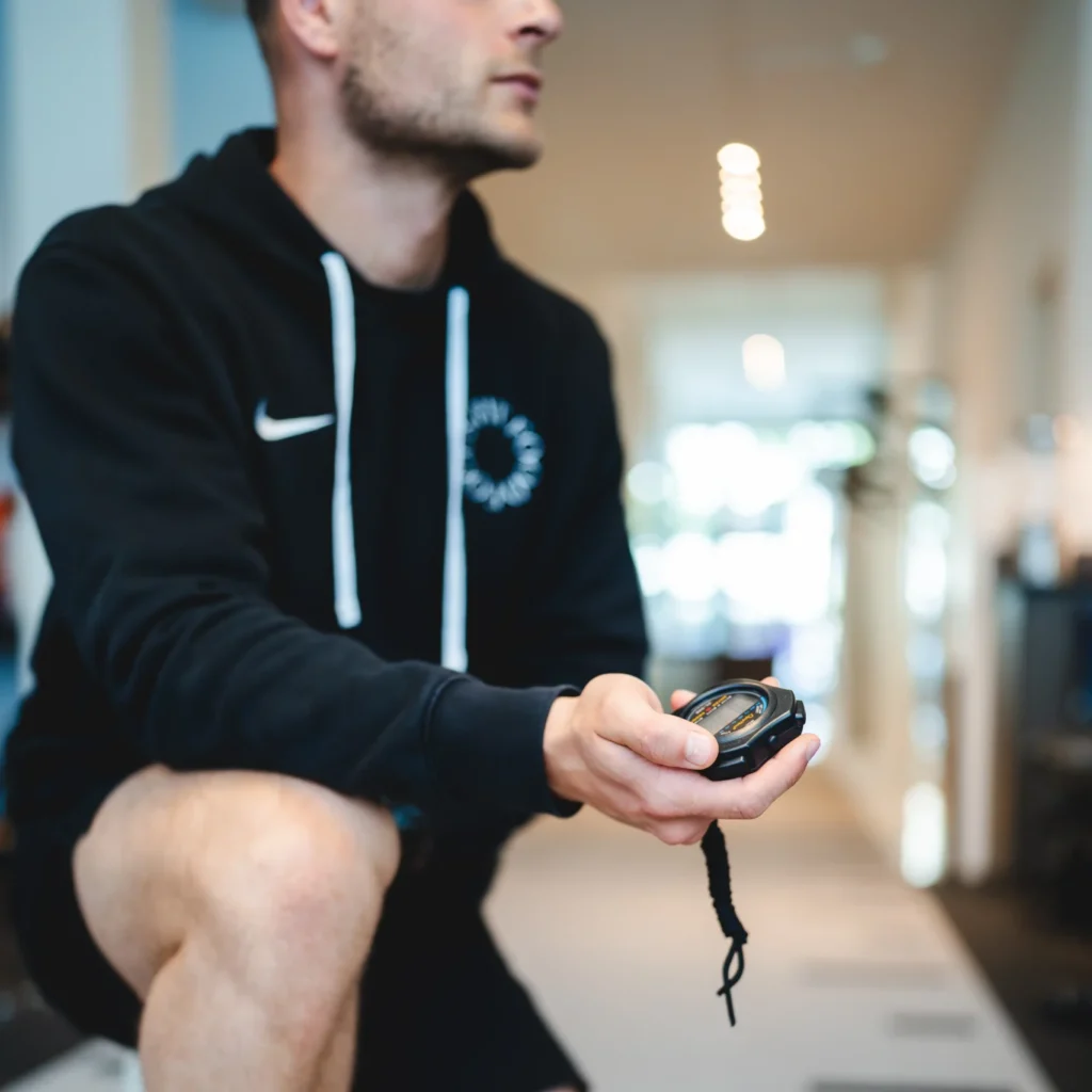 Mannelijke fysiotherapeut met stopwatch in zijn hand voor het timen van een training