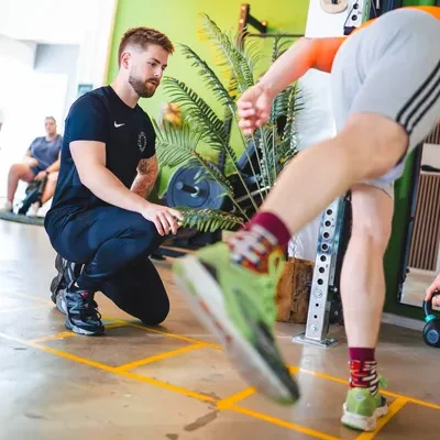 Client doet oefening en staat op 1 been voor corestabiliteit in kleurrijke fitnessruimte onder begeleiding van de F3 fysiotherapeut