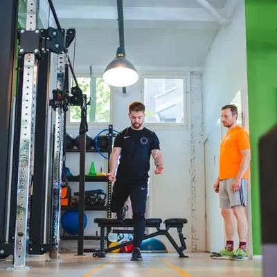 F3 fysiotherapeut staat in lichte moderne fitnessruimte met client en doet evenwichtsoefening voor