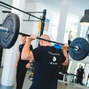 Man legt barbell met gewichten in zijn nek in een lichte en moderne fitnessruimte op de walenburgerweg te Rotterdam
