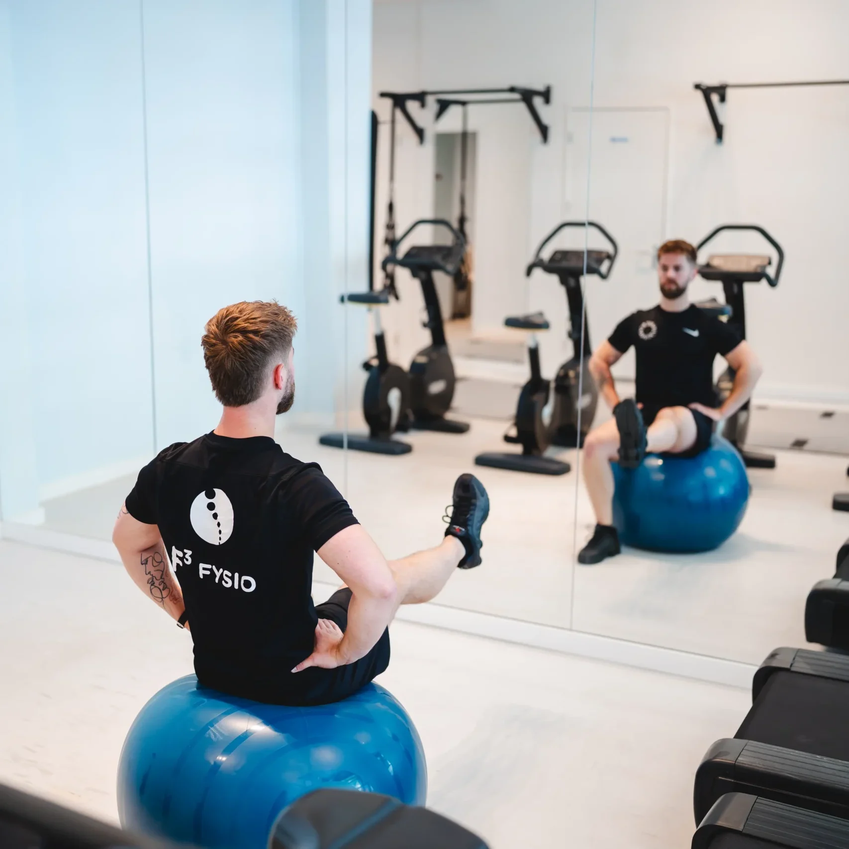 Man doet balansoefening op fitnessbal waarbij hij een been strekt in moderne en lichte fitnessruimte bij F3 Fysio