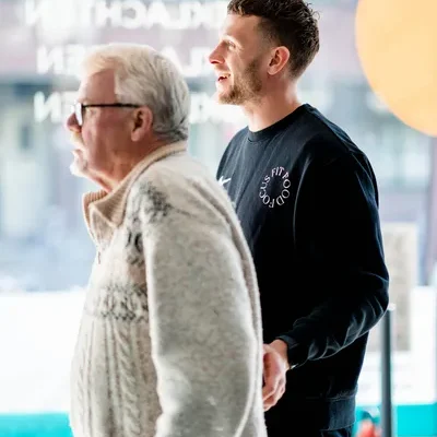 Oudere man met dumbells in zijn hand staat met F3 fysiotherapeut in de vestiging op de schieweg