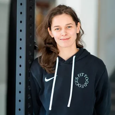 F3 fysiotherapeut Roby staat in fitnessruimte tegen een fitness apparaat geleund