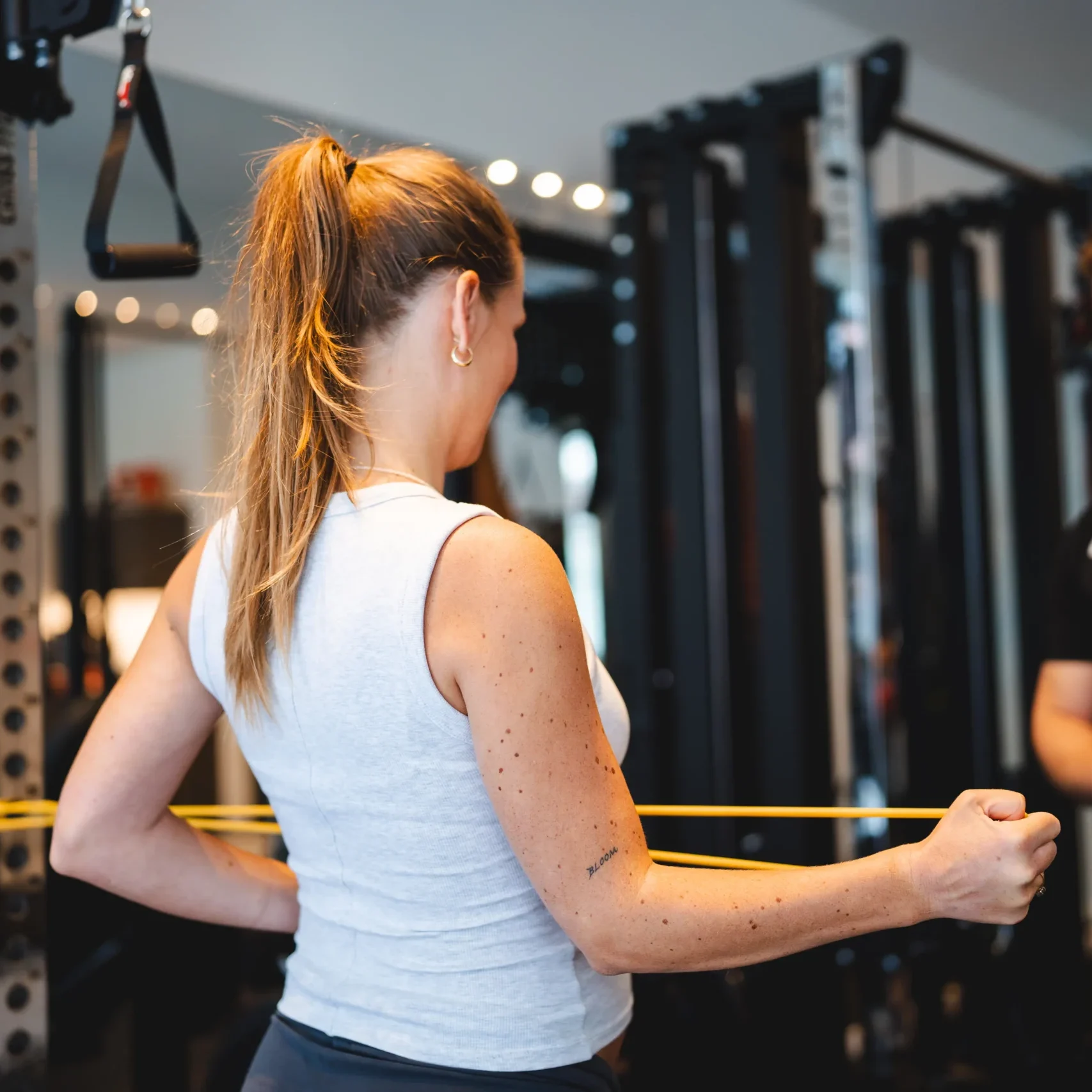 Zwangere vrouw doet schouderoefening met weerstandsband onder begeleiding van de fysiotherapeut in moderne fitnessruimte