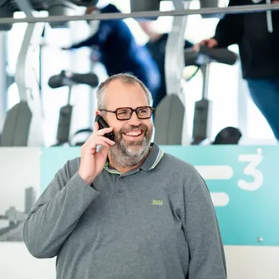 Medewerker F3 fysio staat lachend achter de balie met een telefoon in zijn hand op de walenburgerweg te Rotterdam